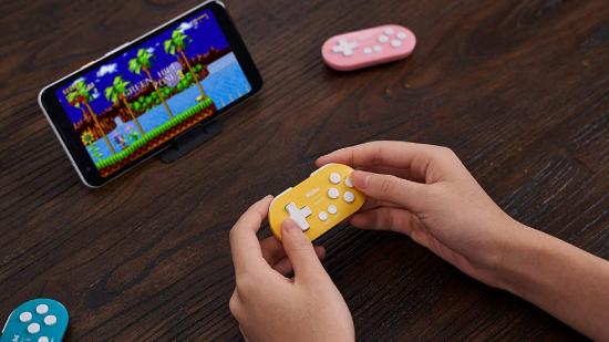 A pair of hands holds a small, yellow, wireless controller while playing Sonic on a mobile device